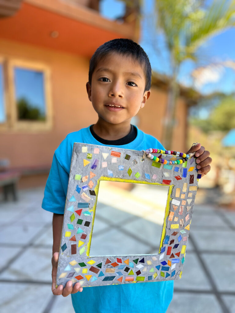 Opal House Summer 25 Preschool Workshop Student holding his mirror and jewelry projects.