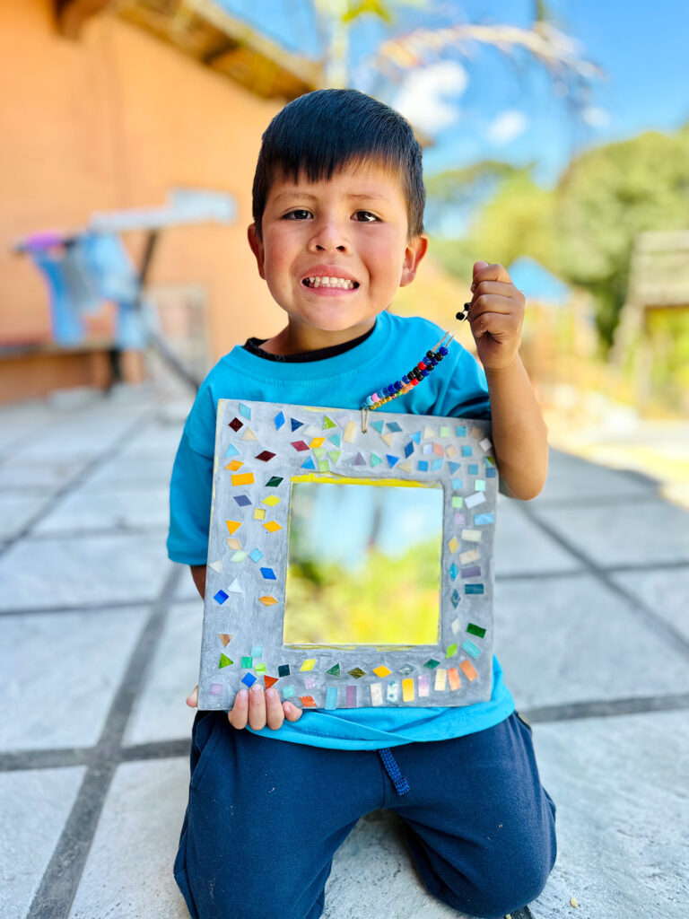 Opal House Summer 25 Preschool Workshop Student holding his mirror and jewelry projects.